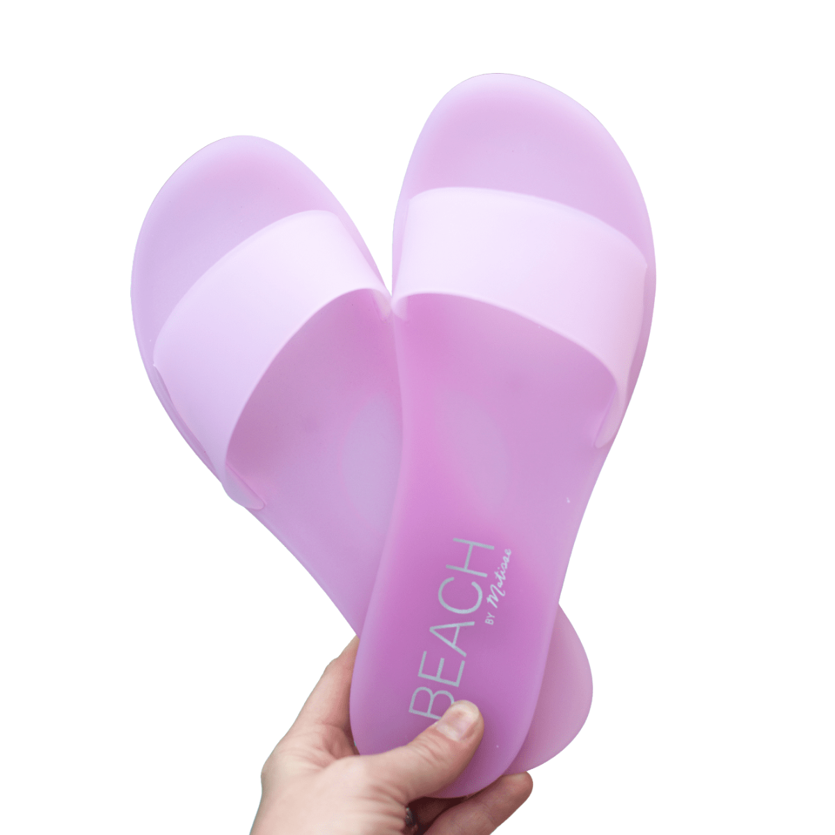 Pink beach sandals with a hand holding them against a white background